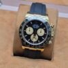 Rolex — cronógrafo con esfera negra y subesferas crema, caja dorada y correa de caucho negra